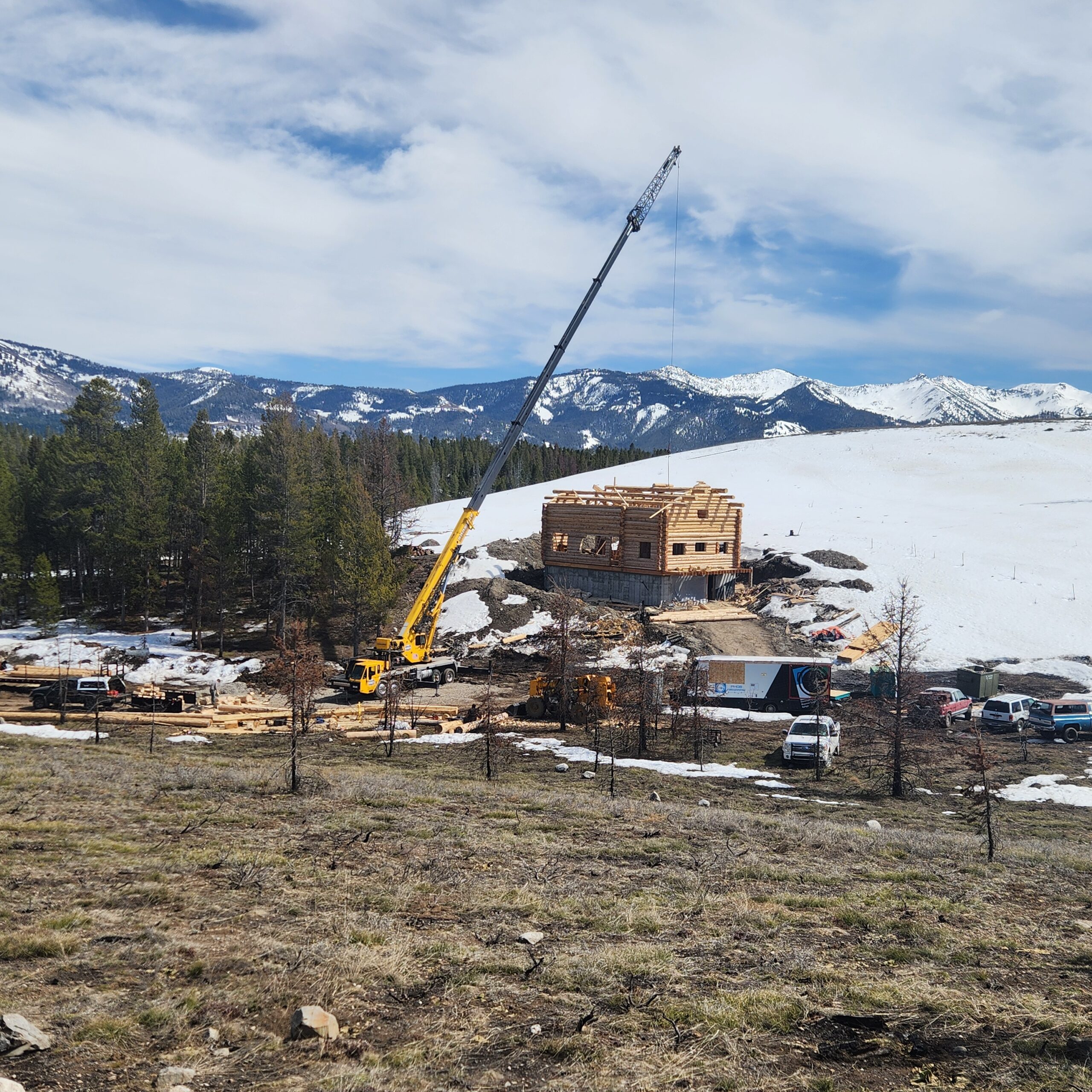 Handcrafted log home construction with crane in a mountain setting