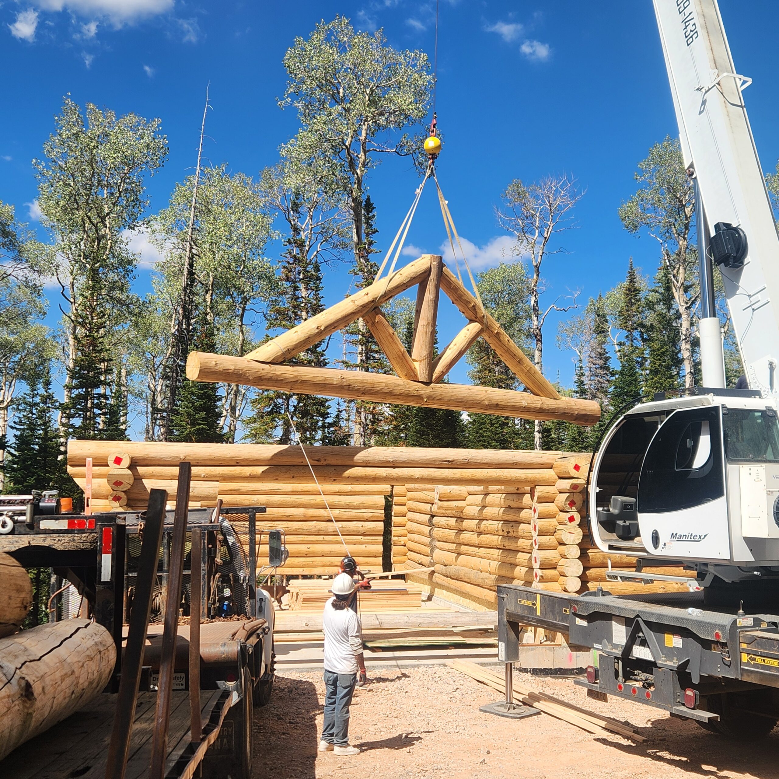 Crane lifting a handcrafted timber truss during log home construction